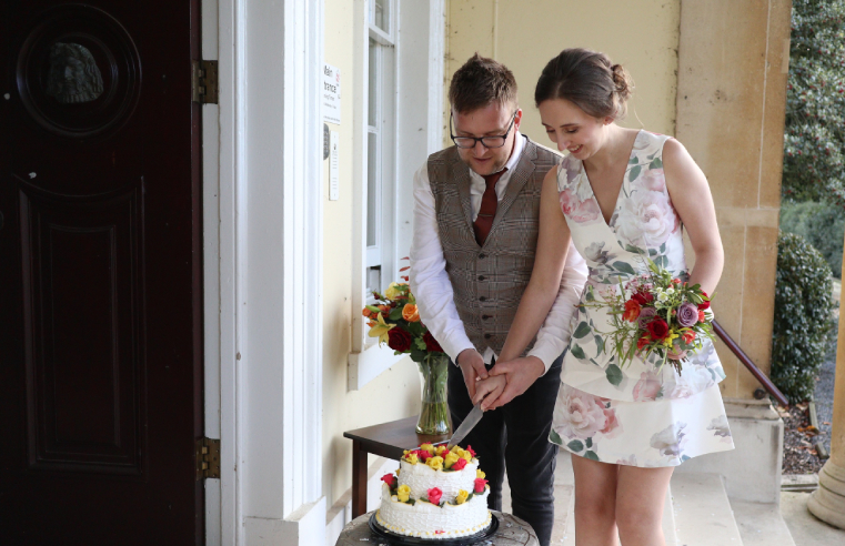 Bride and groom, Kathryn and Tom, cutting their wedding cake outside RMBI Home Prince Edward Duke of Kent Court, while Dot and fellow residents watched them through the window. 